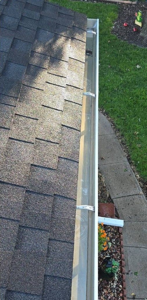 Roof edge with worn shingles, gutter, and a downspout beside a green lawn
