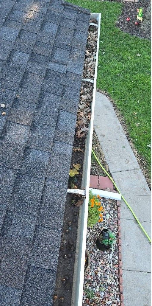 Roof edge with gutter and downspout beside a gravel bed and green lawn