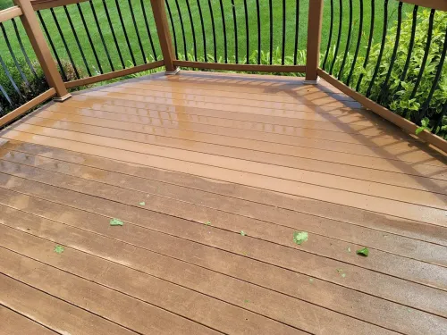 Wooden deck with railing overlooking green lawn, wet with rain and scattered leaves
