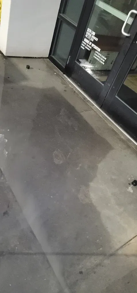 Concrete sidewalk beside a glass storefront with a dark wet stain on the ground