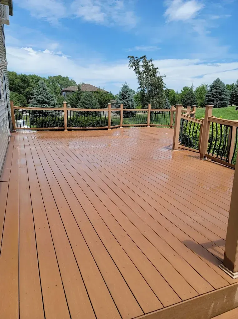 Spacious wooden deck with railings overlooking a green backyard under a blue sky