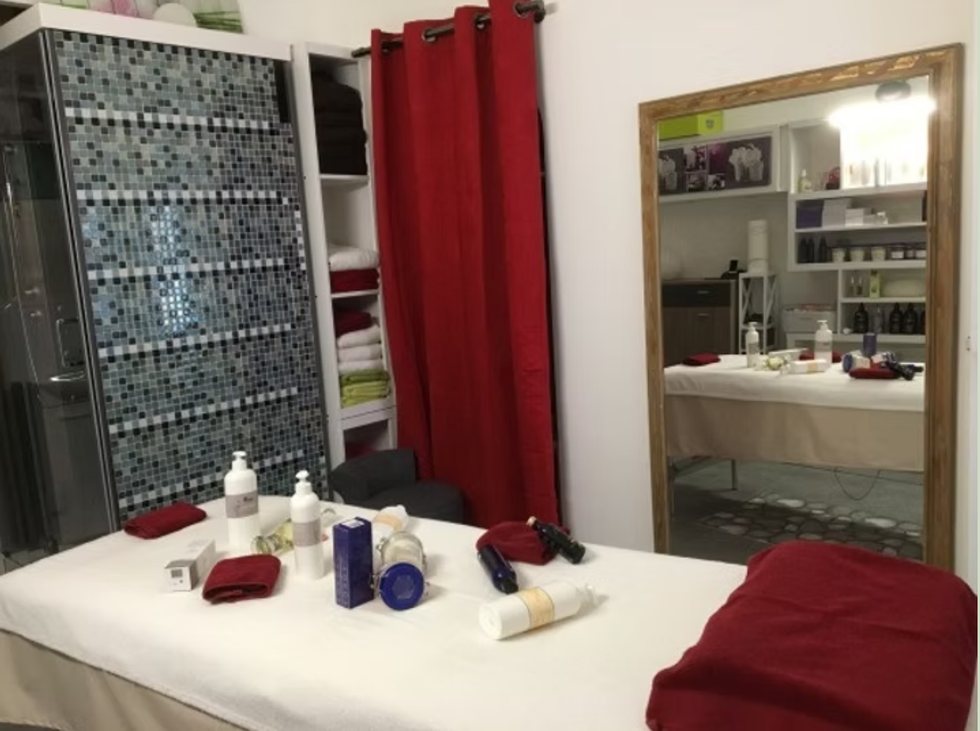 Salle de massage spa avec une table de soin blanche, des serviettes rouges, des bougies et un rideau rouge près d'un miroir.