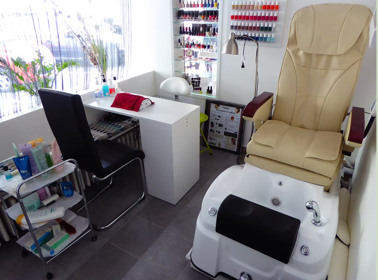 Salon de manucure moderne avec table de manucure, chaise noire, chaise de pédicure beige et présentoir à vernis.