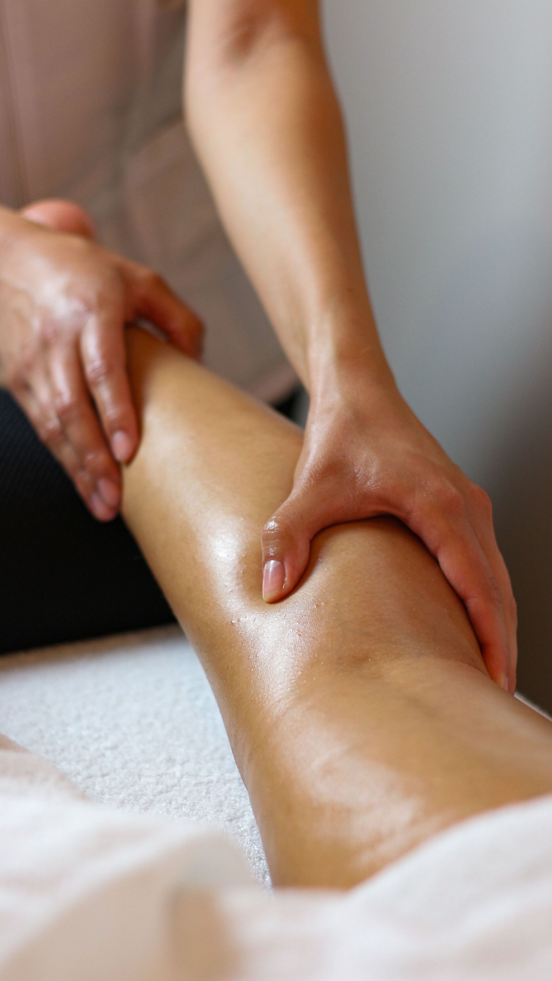 Des mains massent la jambe d'une personne sur une serviette blanche
