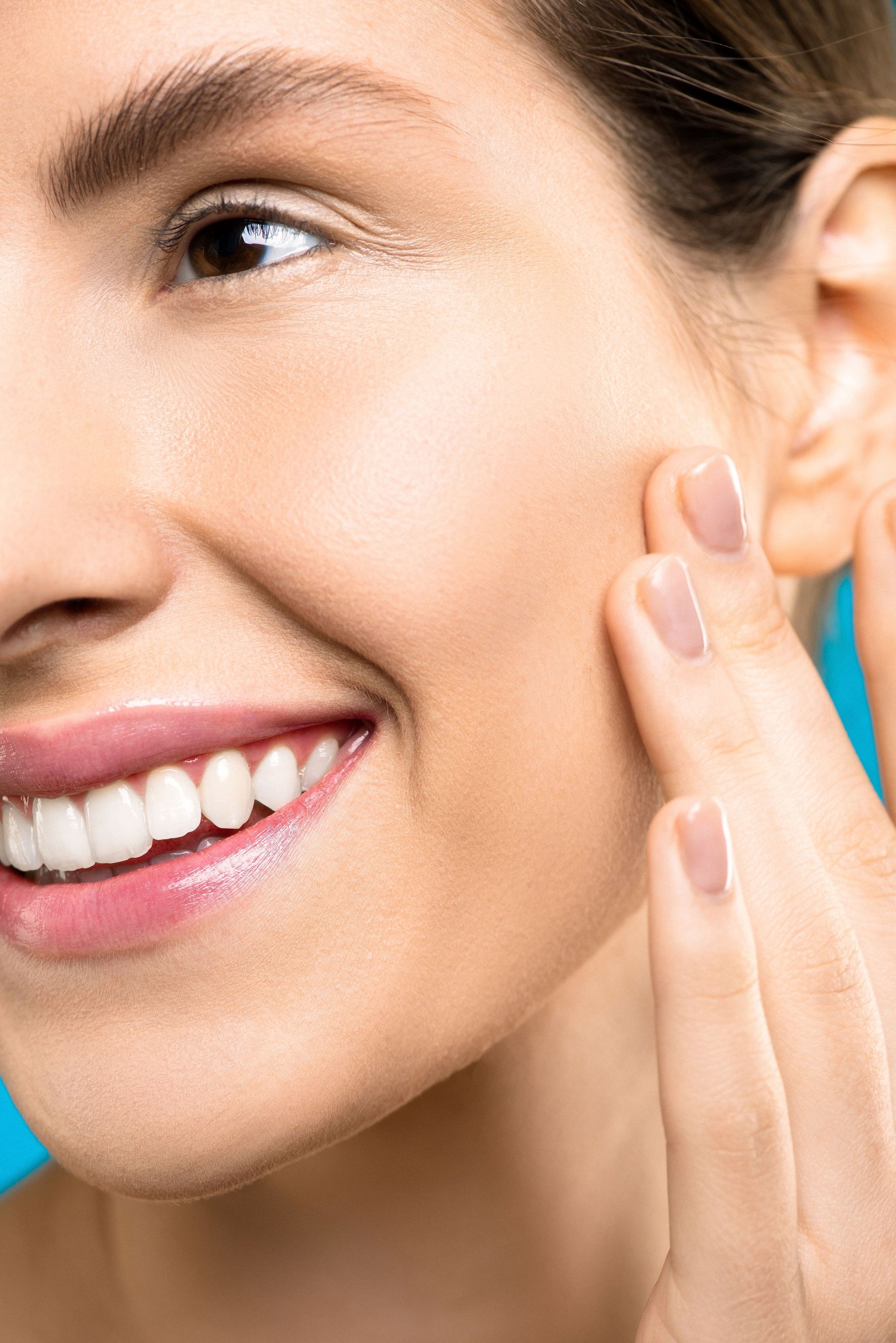 Une femme souriante touche doucement sa joue après avoir appliqué une crème de soin.