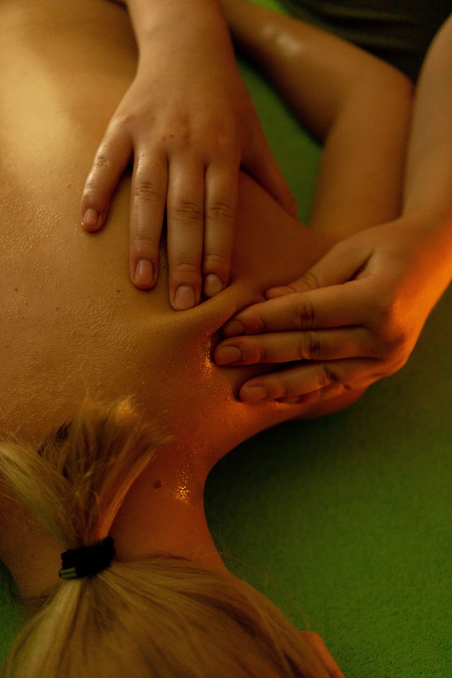 Gros plan sur des mains massant le cou et les épaules d'une personne, vues de dessus ; on aperçoit des cheveux blonds.