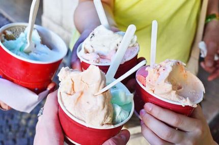 Hands holding colorful cups of ice cream with spoons outdoors