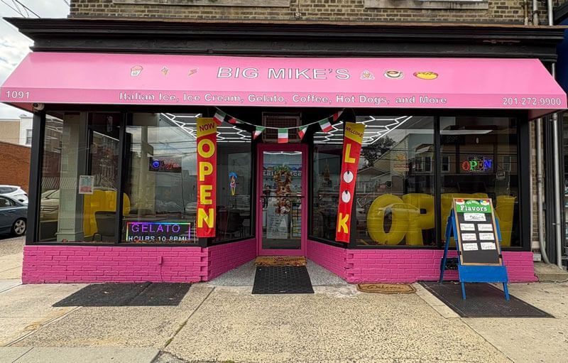 Pink storefront with open sign, large front windows, and sidewalk display outside