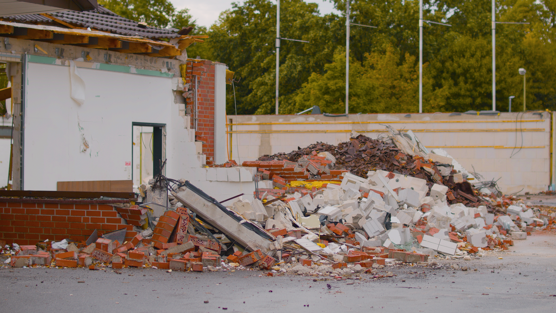 Demolition rubble piled beside a damaged brick building and wall, with debris scattered on the ground