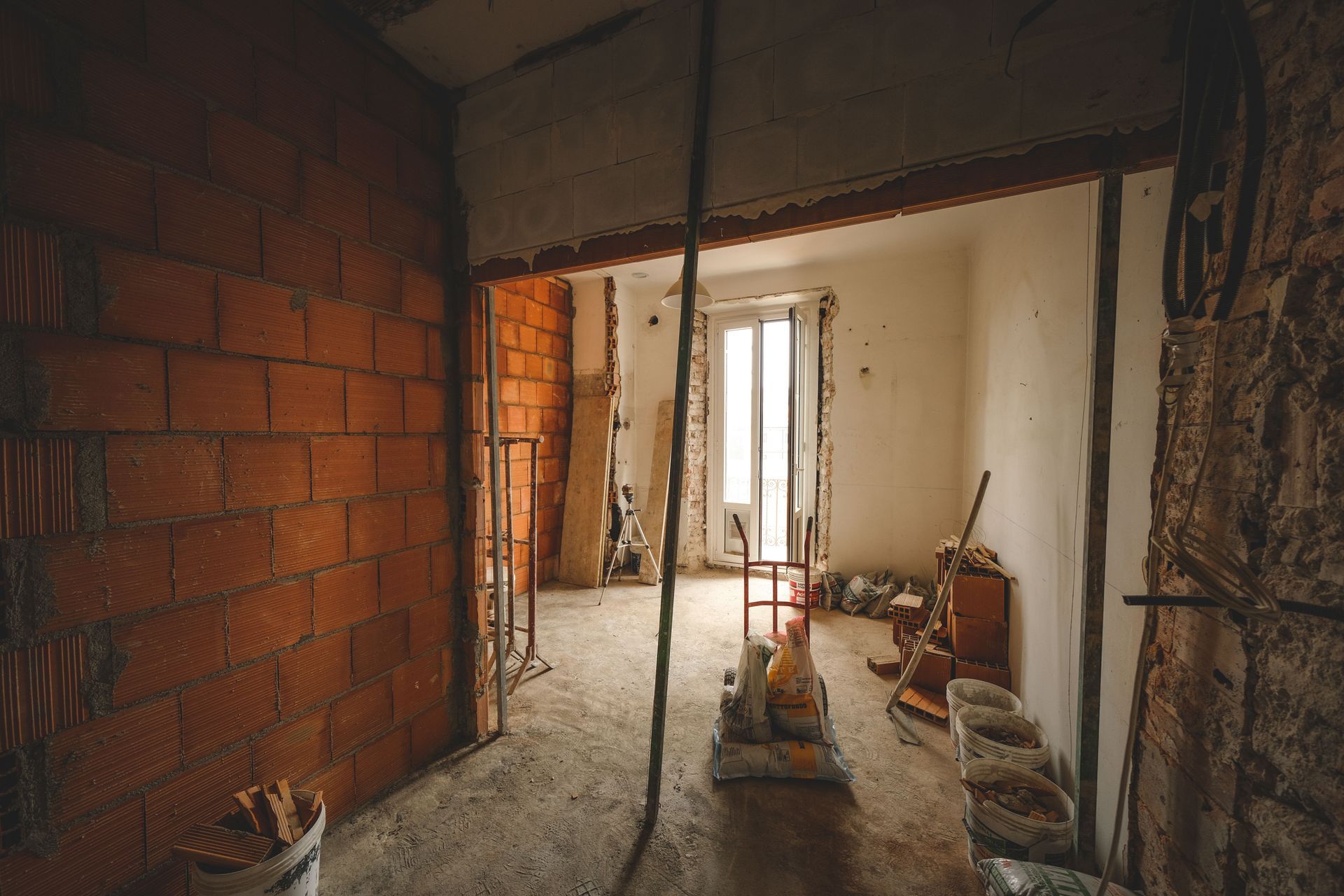 Partially renovated room with exposed brick, unfinished walls, construction tools, and buckets on the floor
