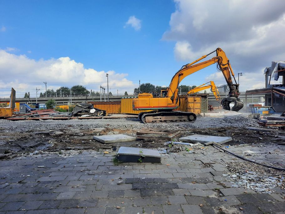 Construction site with orange excavator clearing rubble under a cloudy sky