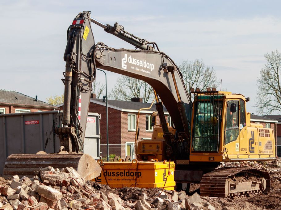 Yellow excavator demolishing a brick structure on a construction site under a clear sky