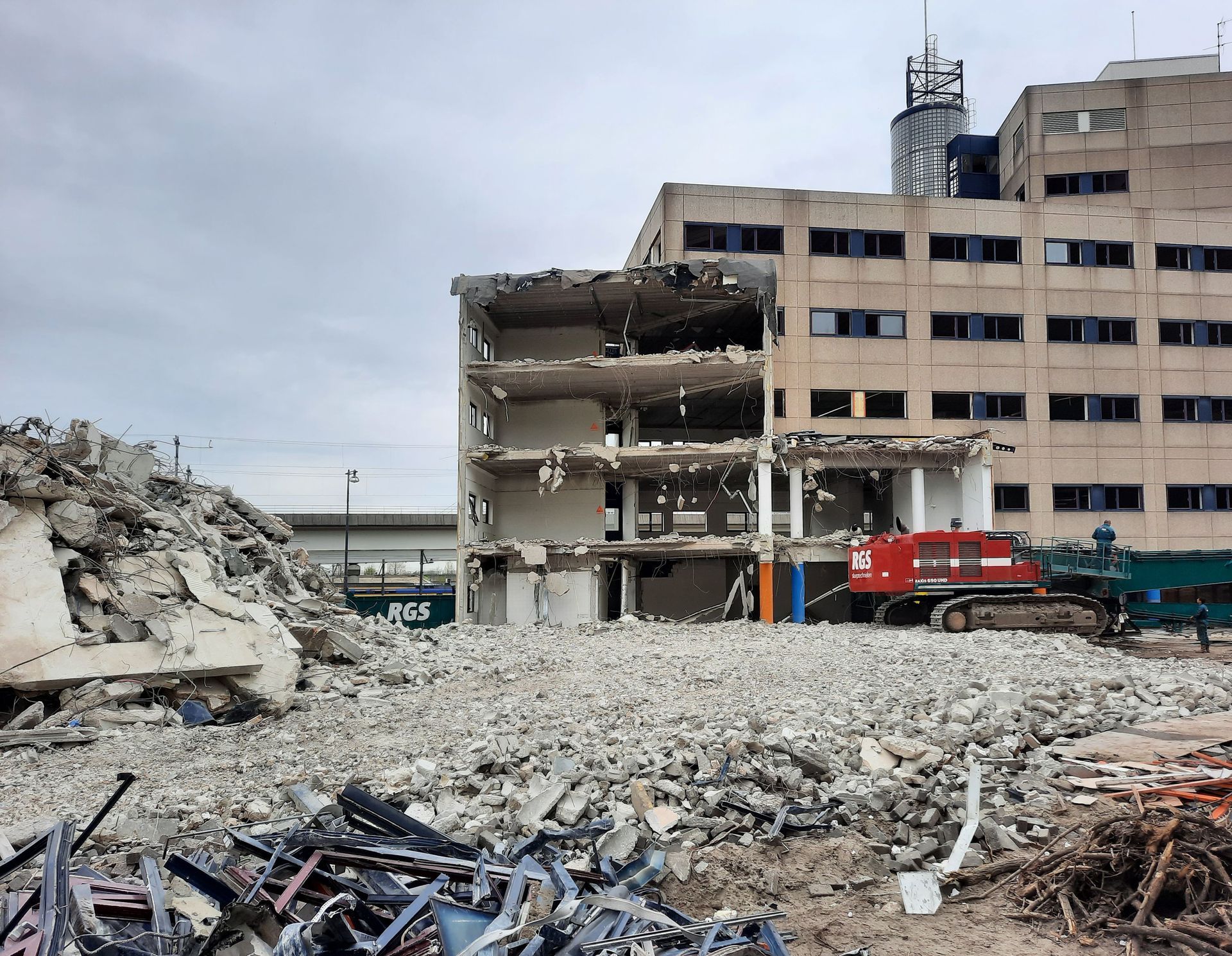Damaged building with rubble and a red excavator at a demolition site