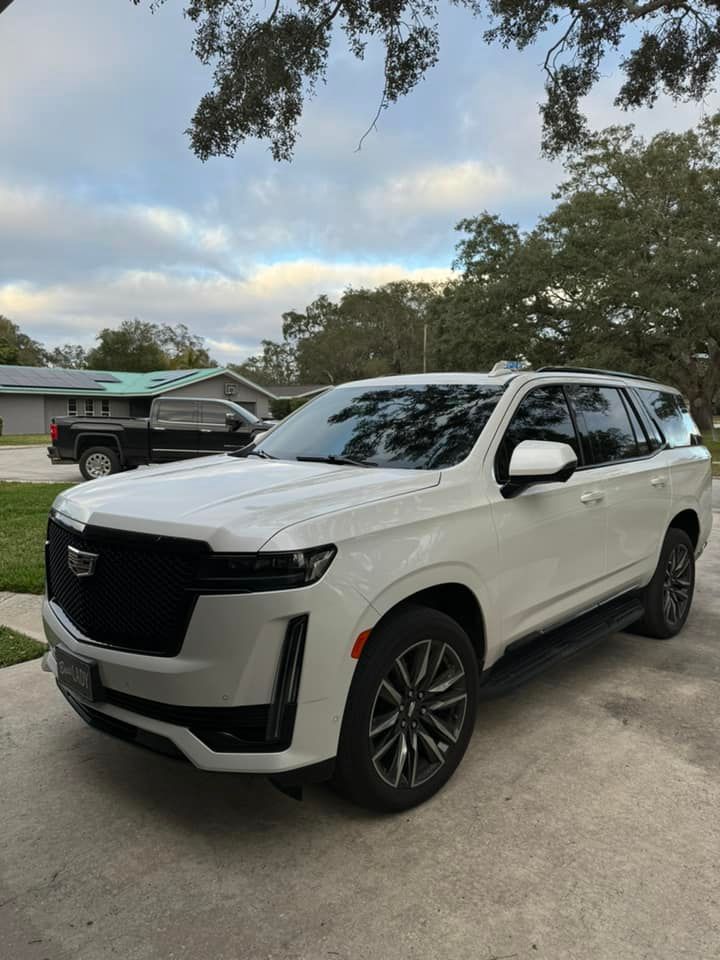 White Cadillac Escalade SUV parked in driveway. Cloudy sky background.