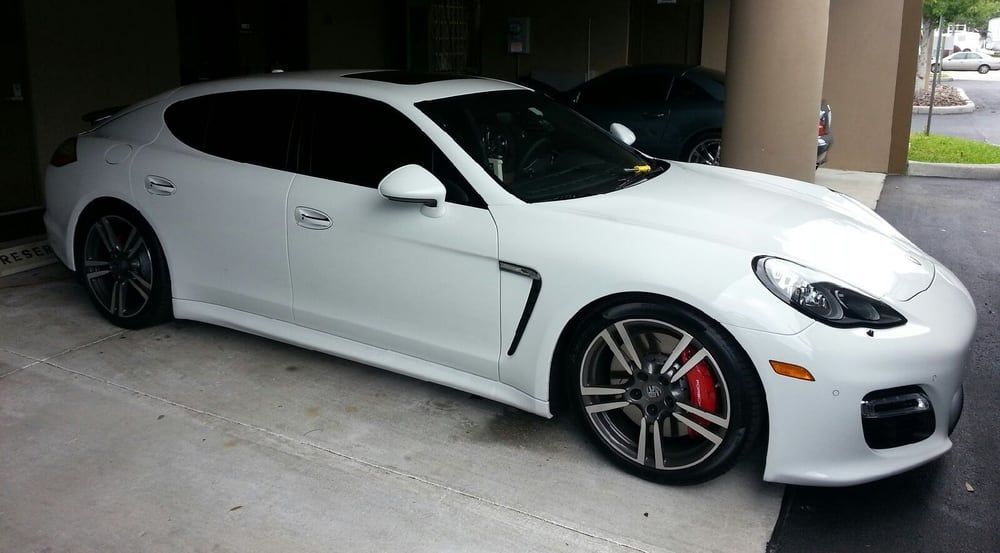 White Porsche Panamera parked under a building overhang; dark tinted windows, red brake calipers.
