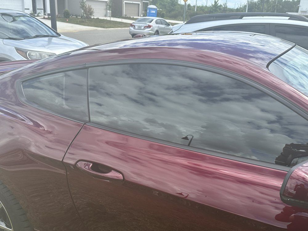 Red sports car, tinted windows, parked outdoors. Reflected cloudy sky.