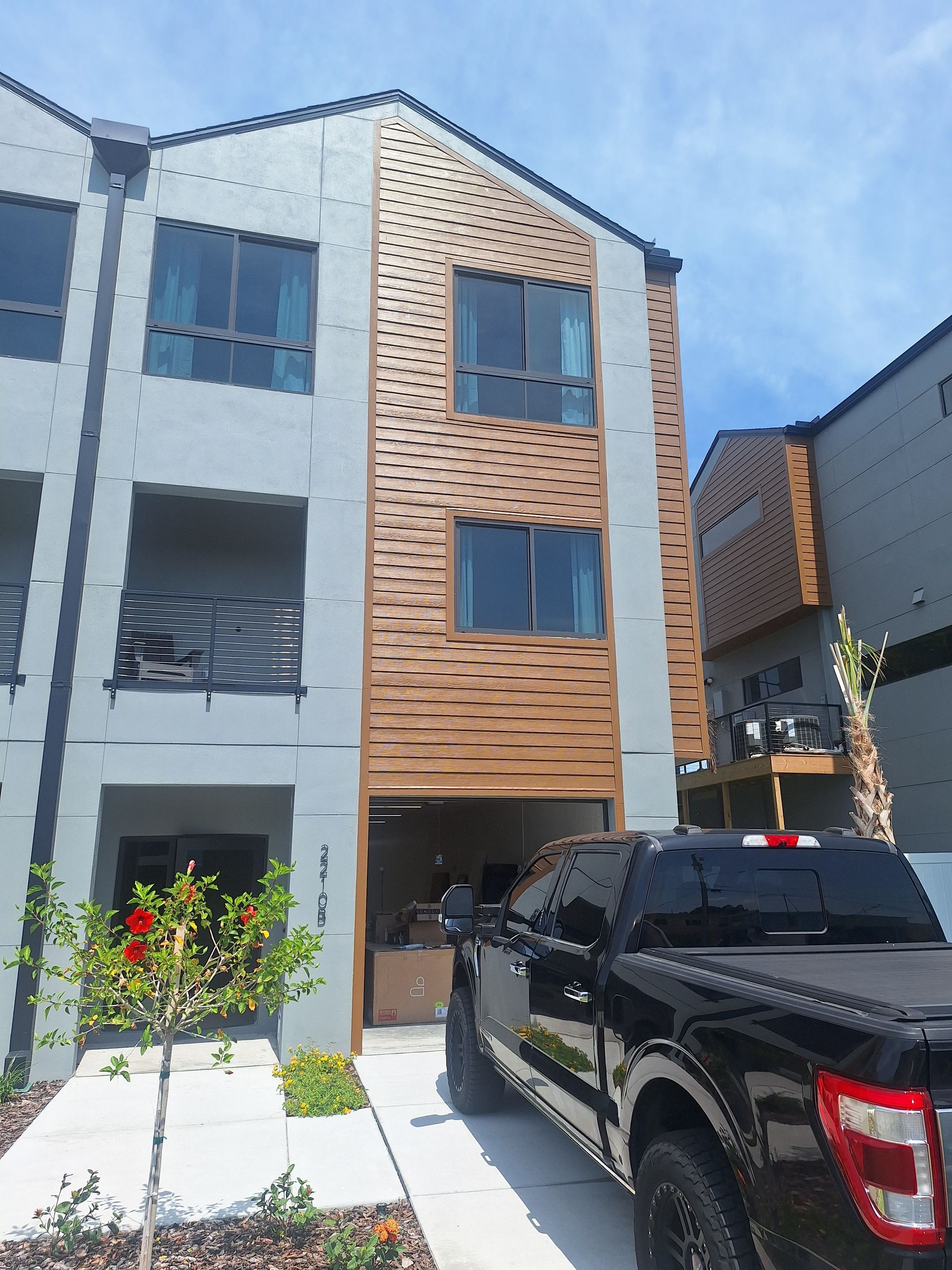 Three-story townhome with grey stucco exterior, wood accents, and a black truck parked in front.