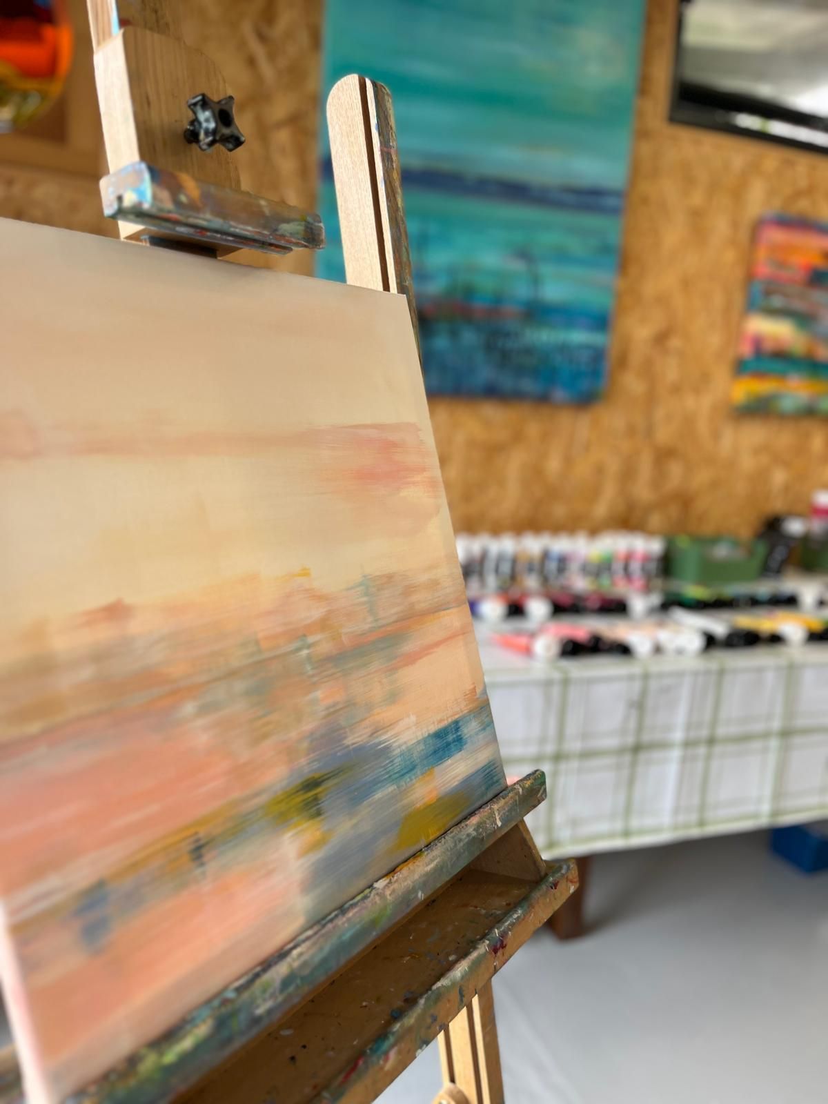 Painting on an easel with blurred brushstrokes in pink, yellow, and blue. Artwork in a studio setting.