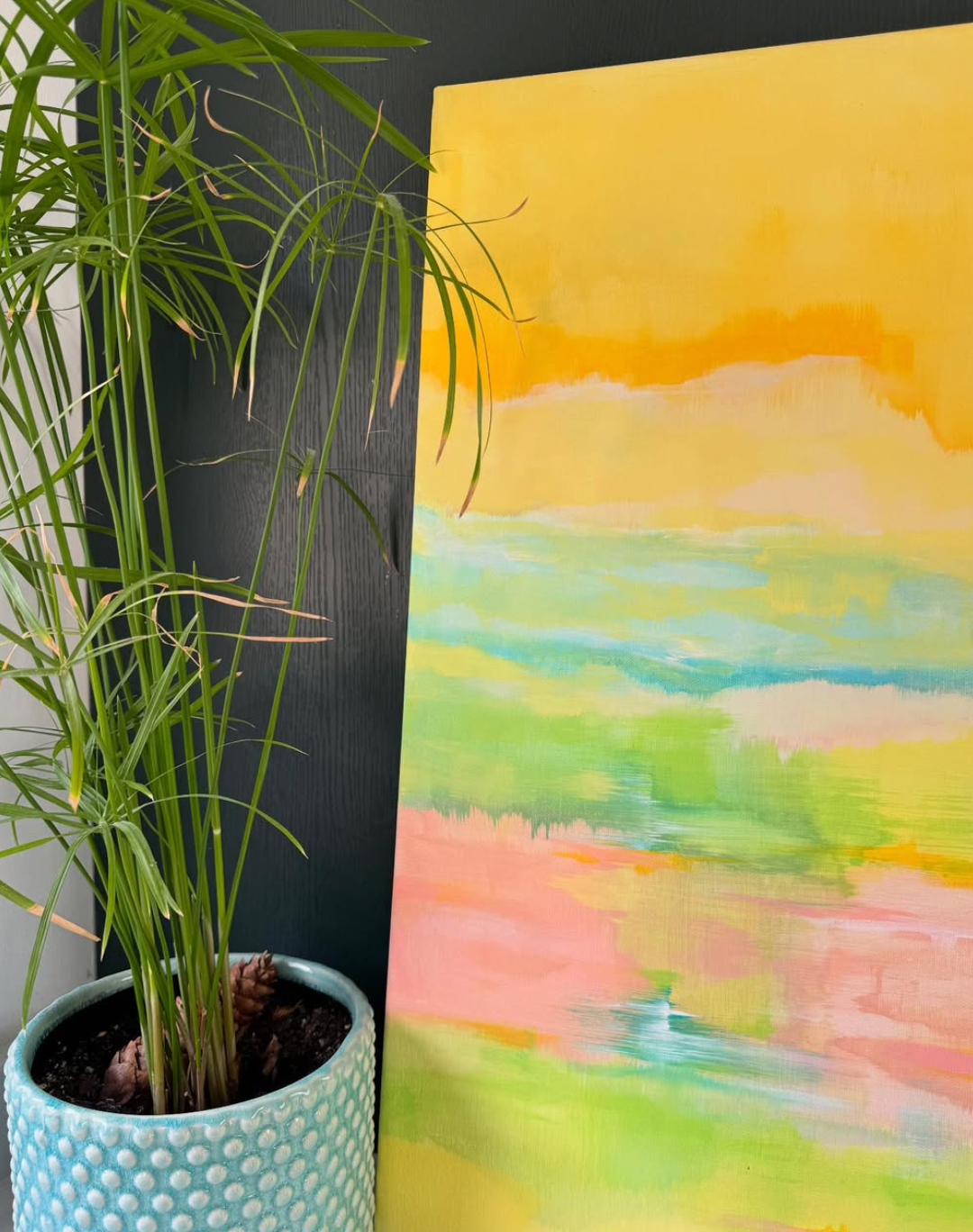 Yellow and pastel abstract painting next to a potted bamboo palm.