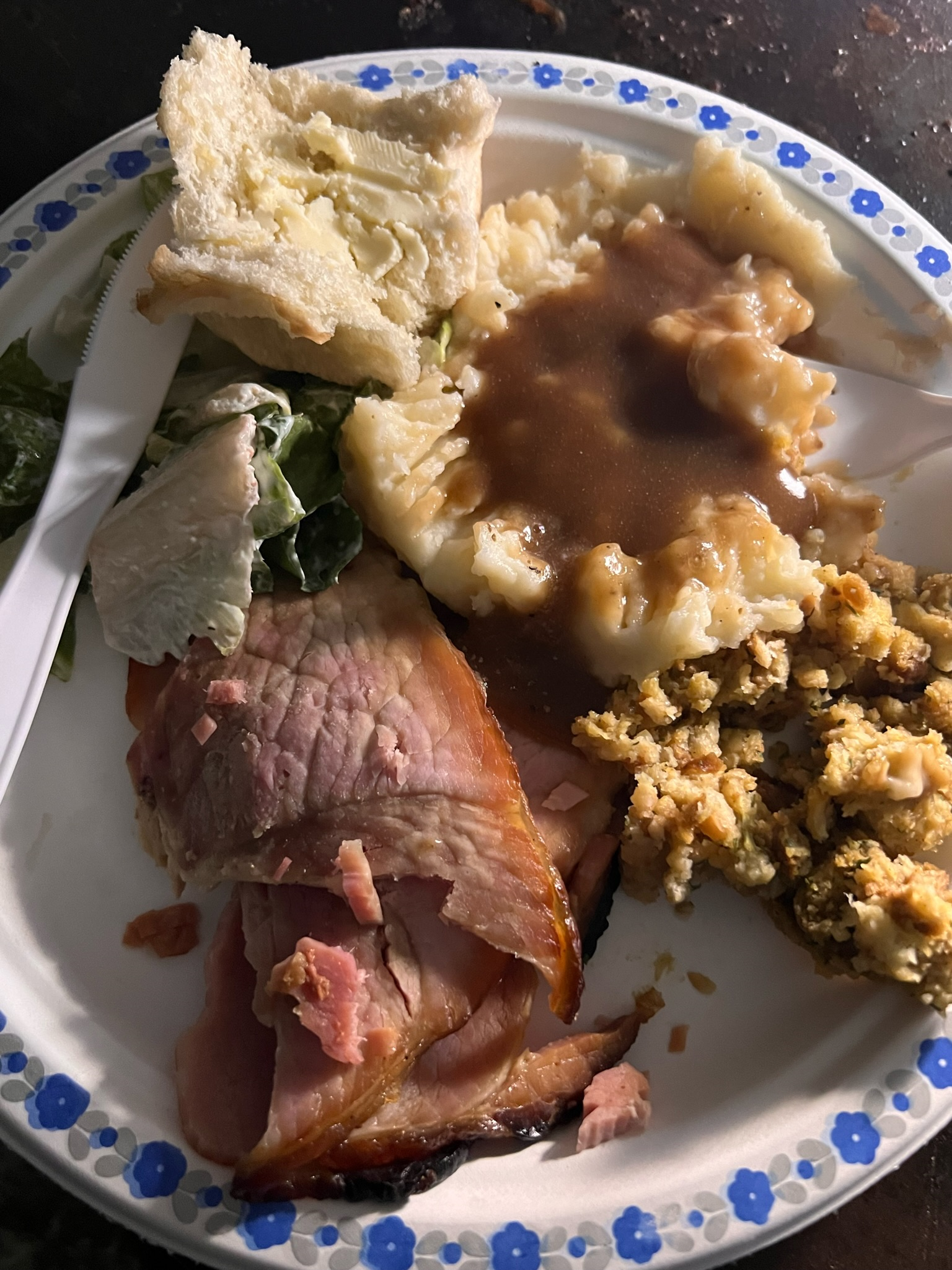 Plate of ham, mashed potatoes with gravy, stuffing, and bread.