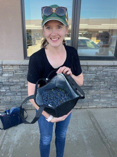 Woman holding open insulated tote bag filled with blueberries, smiling outside.
