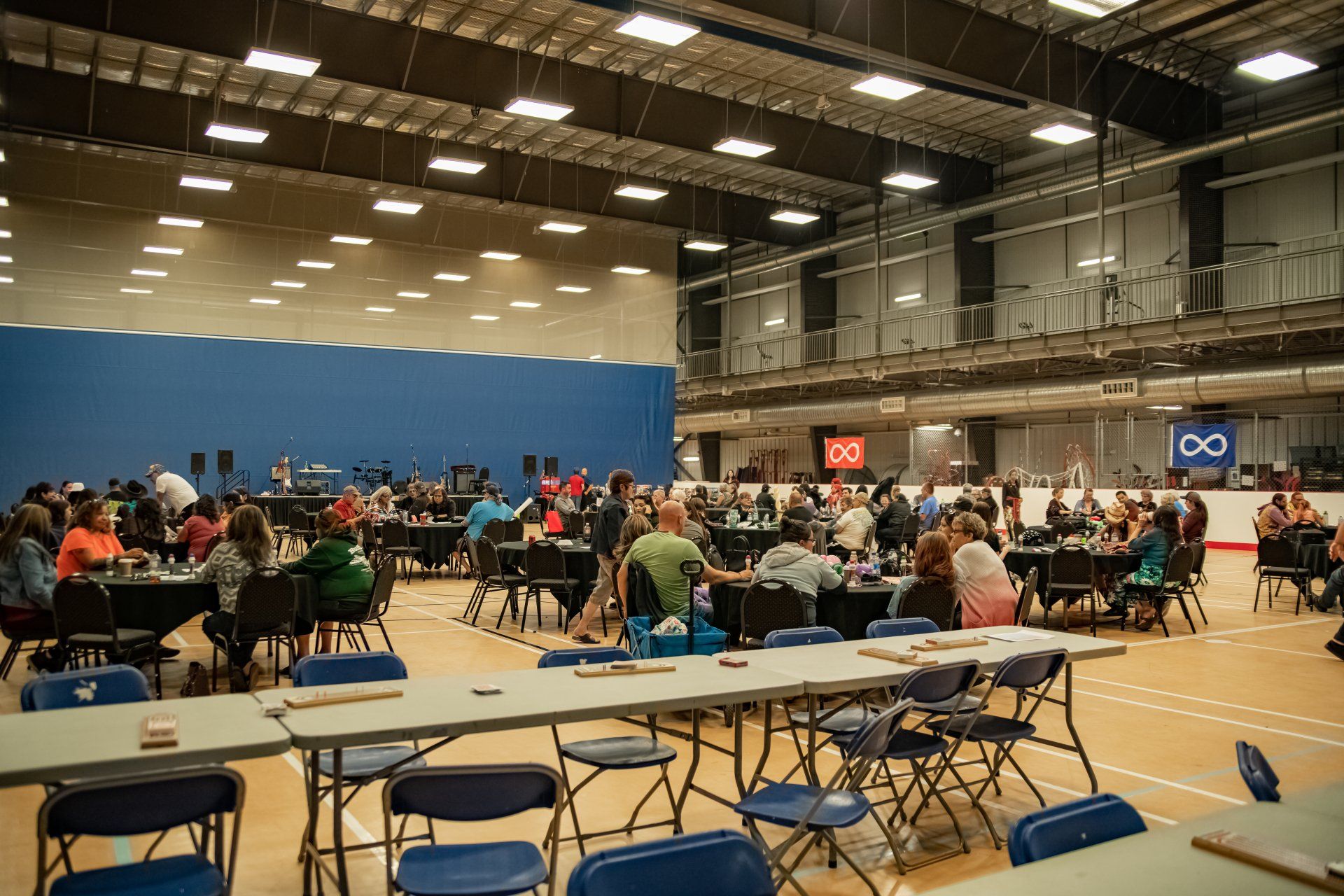 Large event hall with many people at tables, blue wall, indoor.