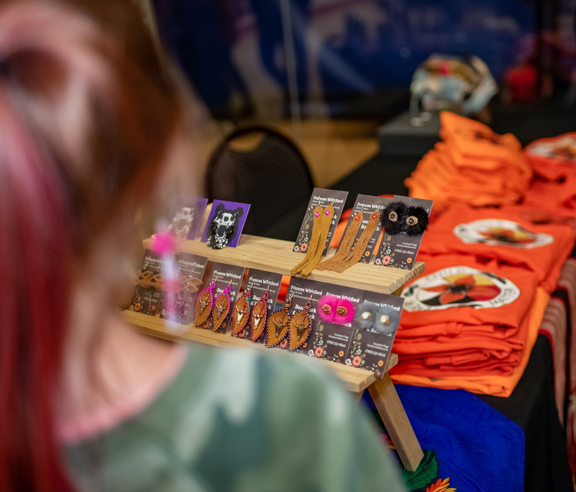 Person looking at a display of earrings. Orange t-shirts are in the background.