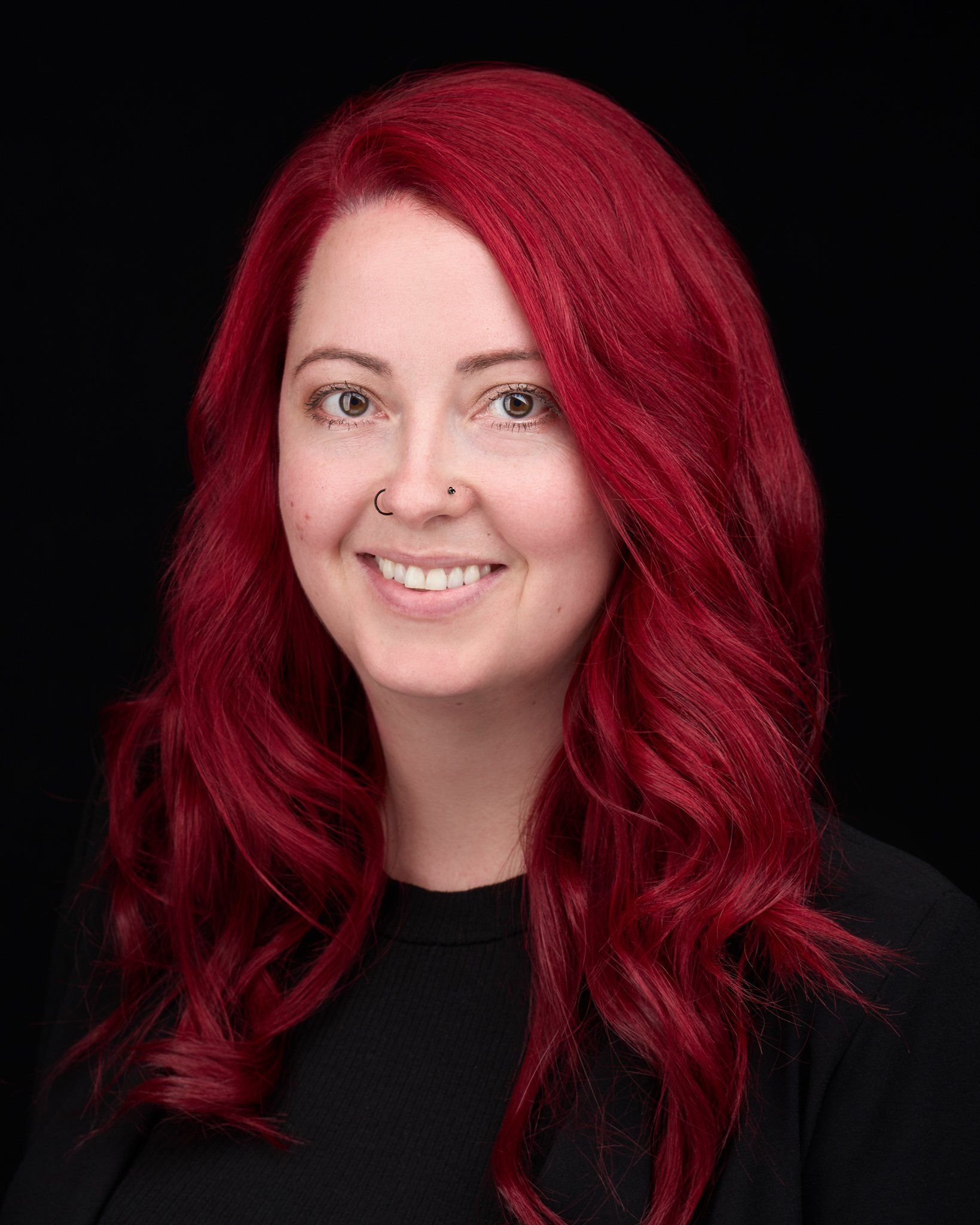 Woman with red hair smiles at the camera against a black background.