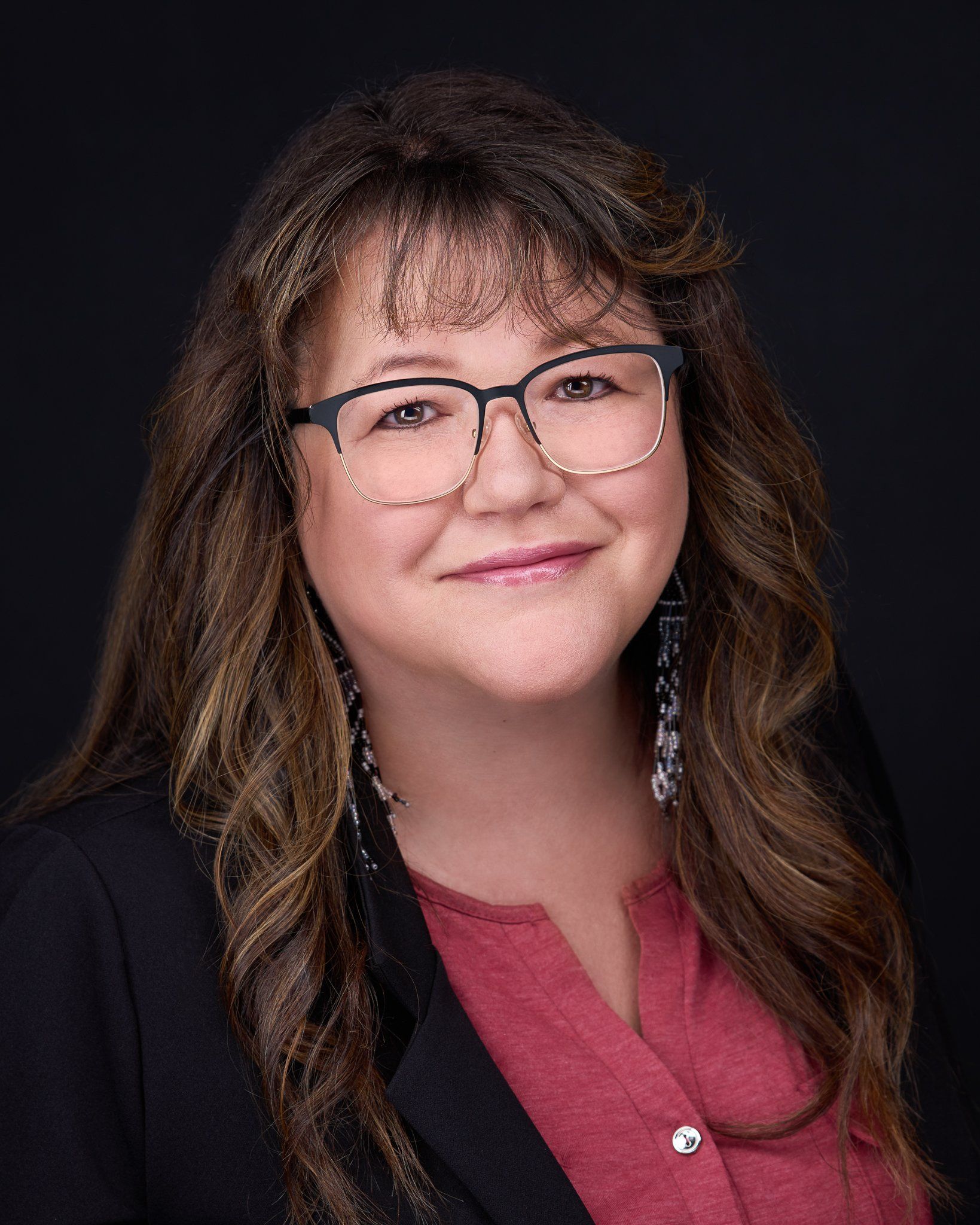 Woman with glasses, long brown hair, wearing a red shirt and black blazer, smiling at the camera.