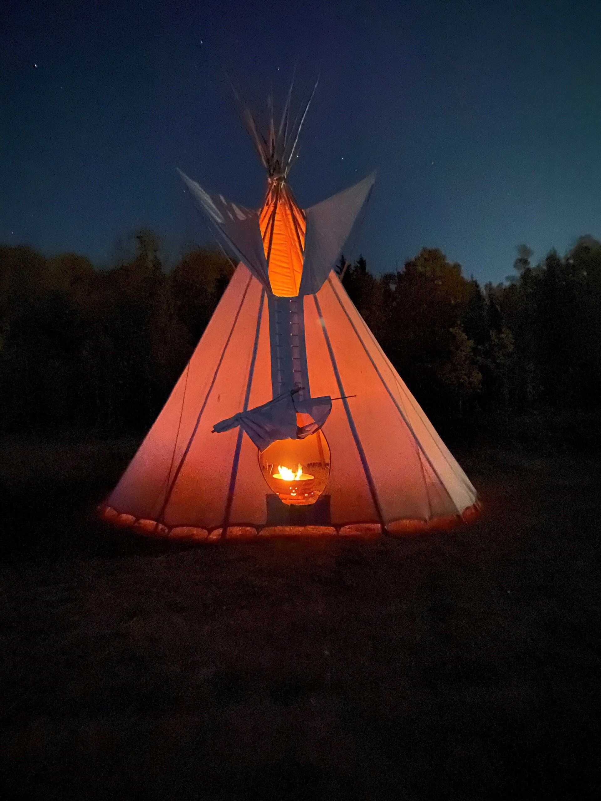 Lit up teepee at night with an orange glow and flames visible at the bottom.