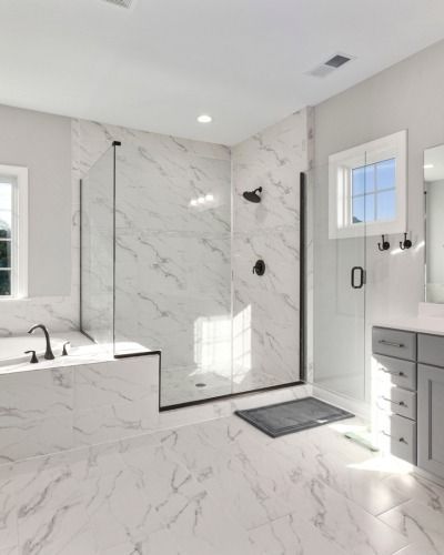 Bright marble-tiled bathroom with walk-in shower, tub, vanity, and glass door.