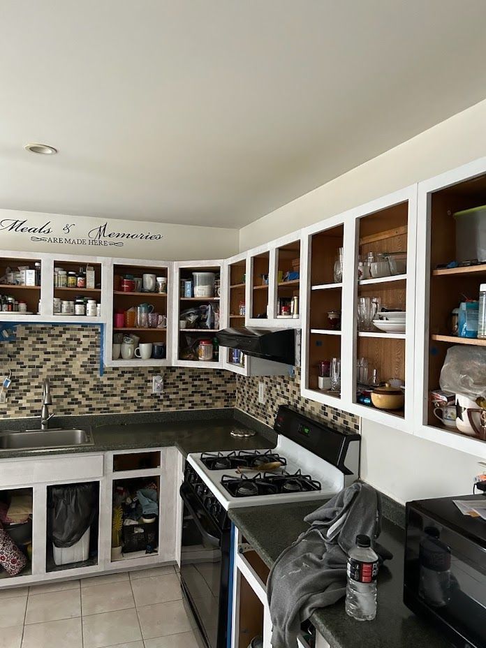 Modern kitchen with white cabinets, stone backsplash, black countertops, and a gas stove.