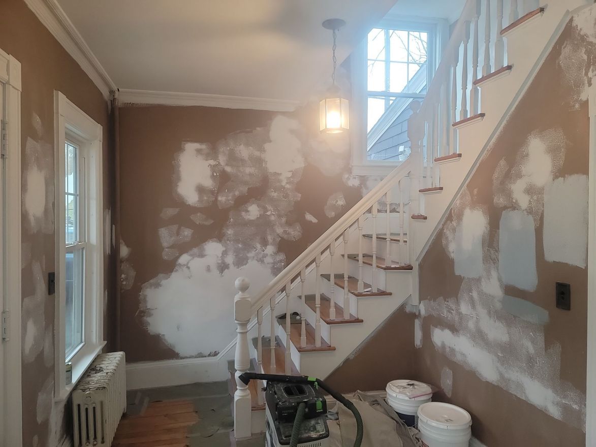 Partially renovated stairway hallway with patchy drywall, paint, and tools on the floor