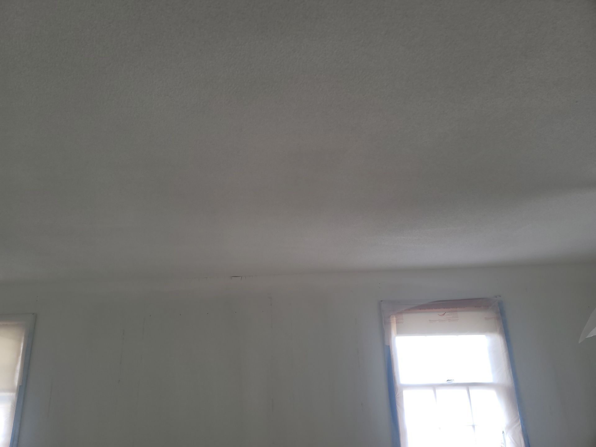 Plain white room ceiling with two windows letting in daylight