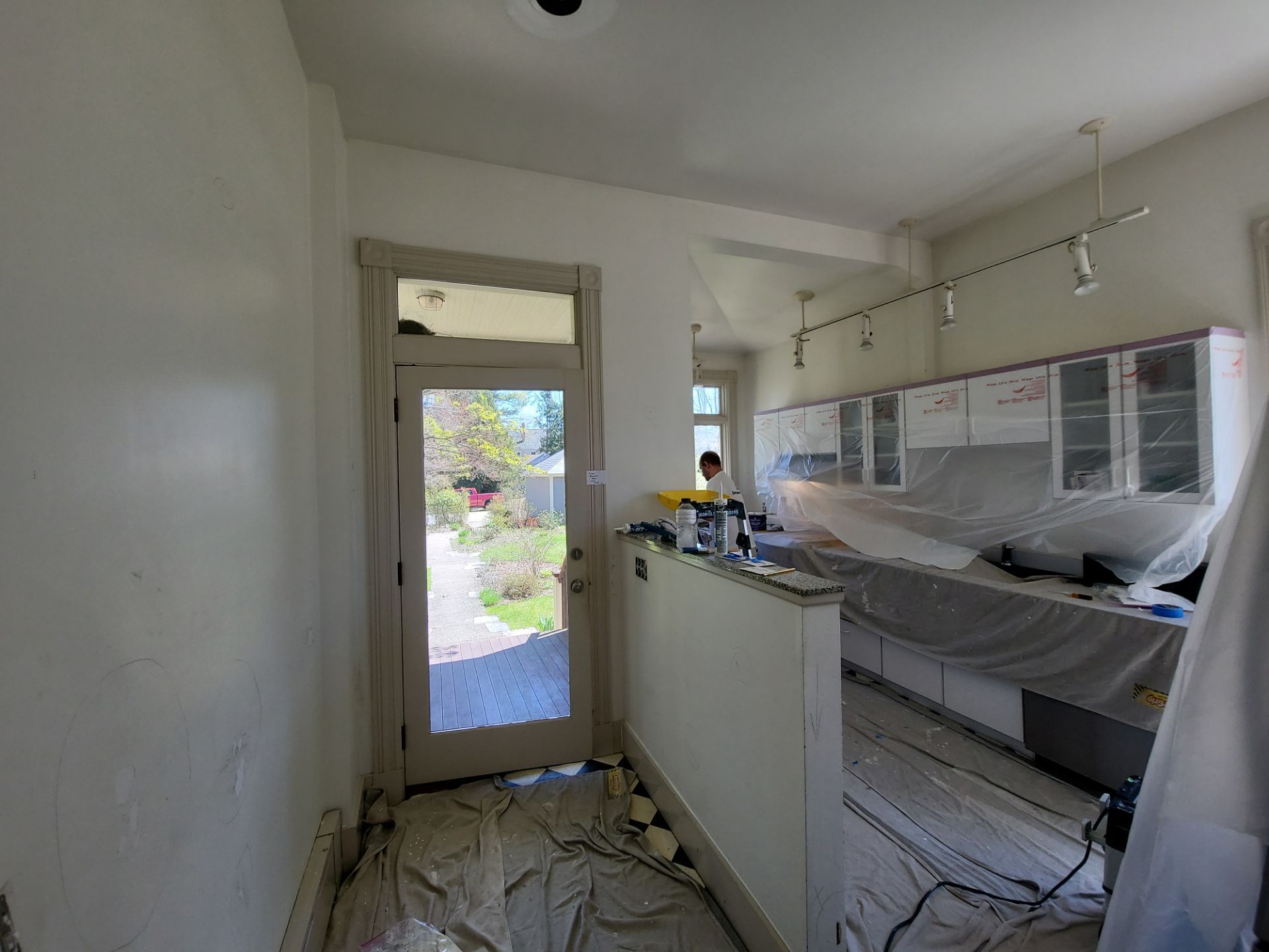 Narrow kitchen under renovation with white cabinets, covered counters, and debris on the floor.