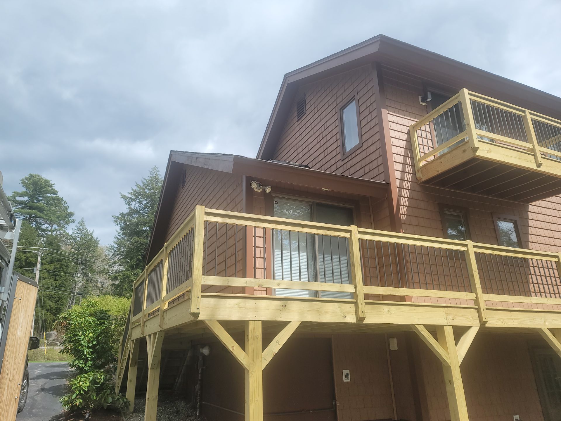 Two-story brown house with yellow wooden deck and stairs, under a cloudy sky