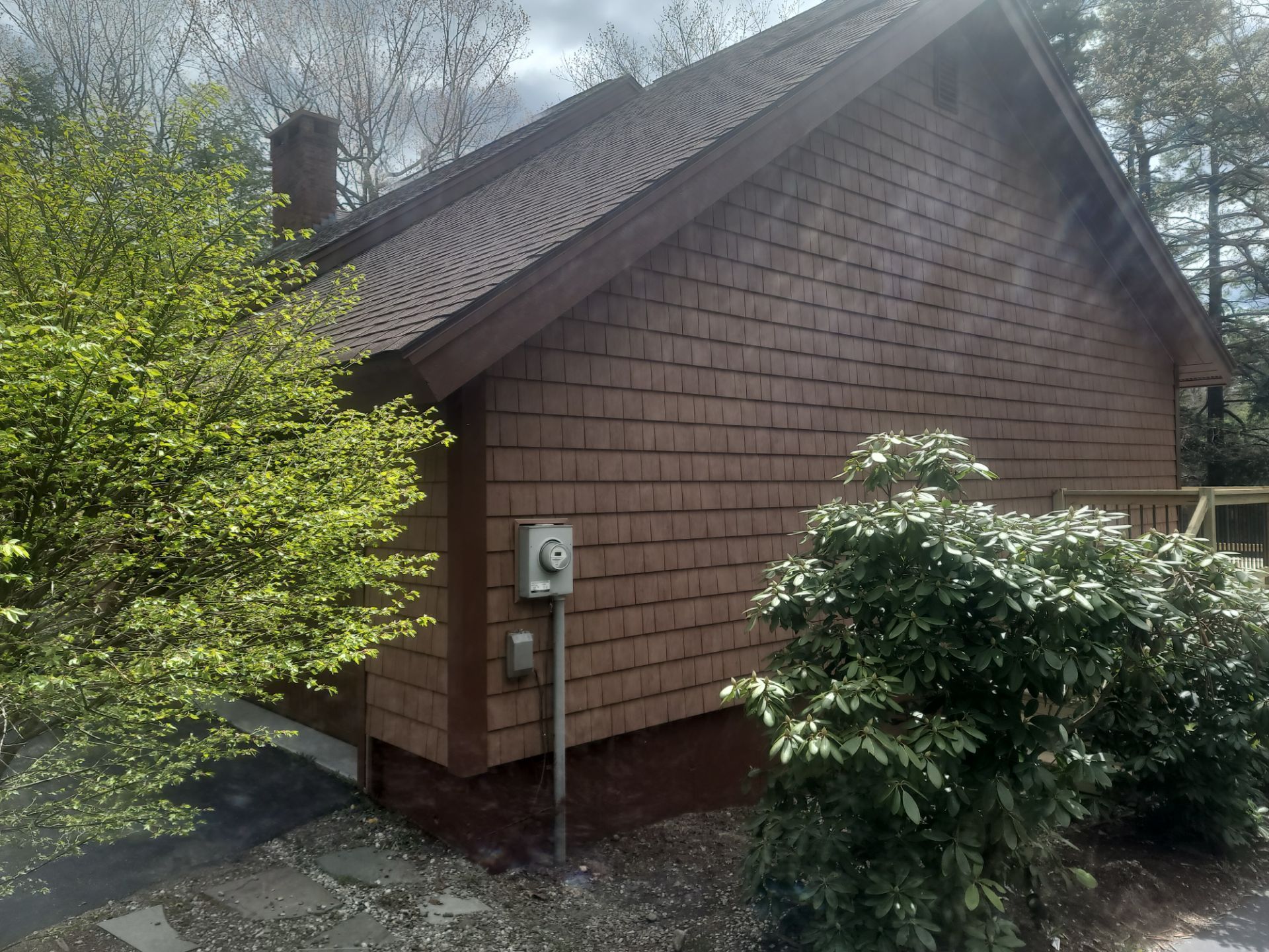Brown shingled house exterior with bushes and trees in bright daylight