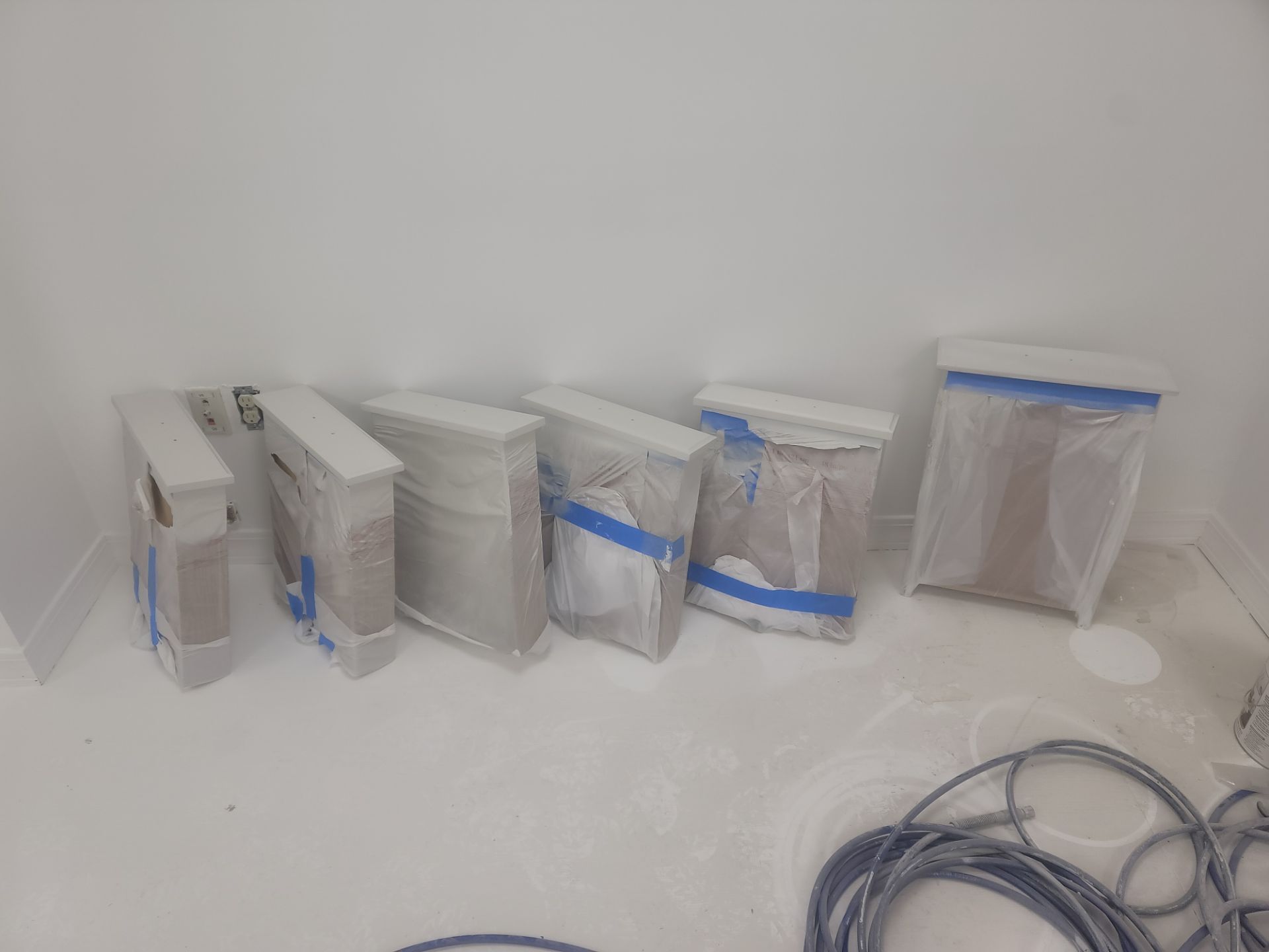 Several small objects wrapped in plastic and taped, lined up on a white shelf or table.