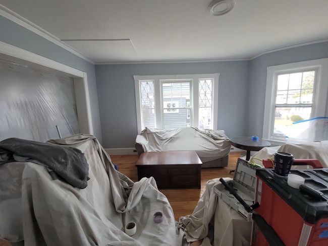 Gray living room with furniture covered in plastic and supplies, suggesting an in-progress move or renovation