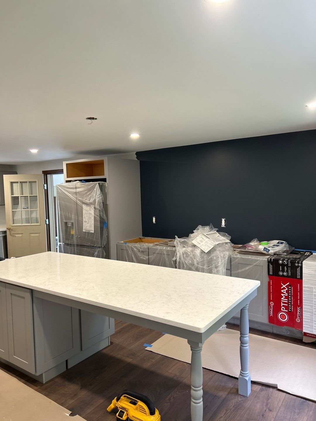 Kitchen under renovation with island, covered appliances, dark accent wall, and a Coca-Cola carton on the counter