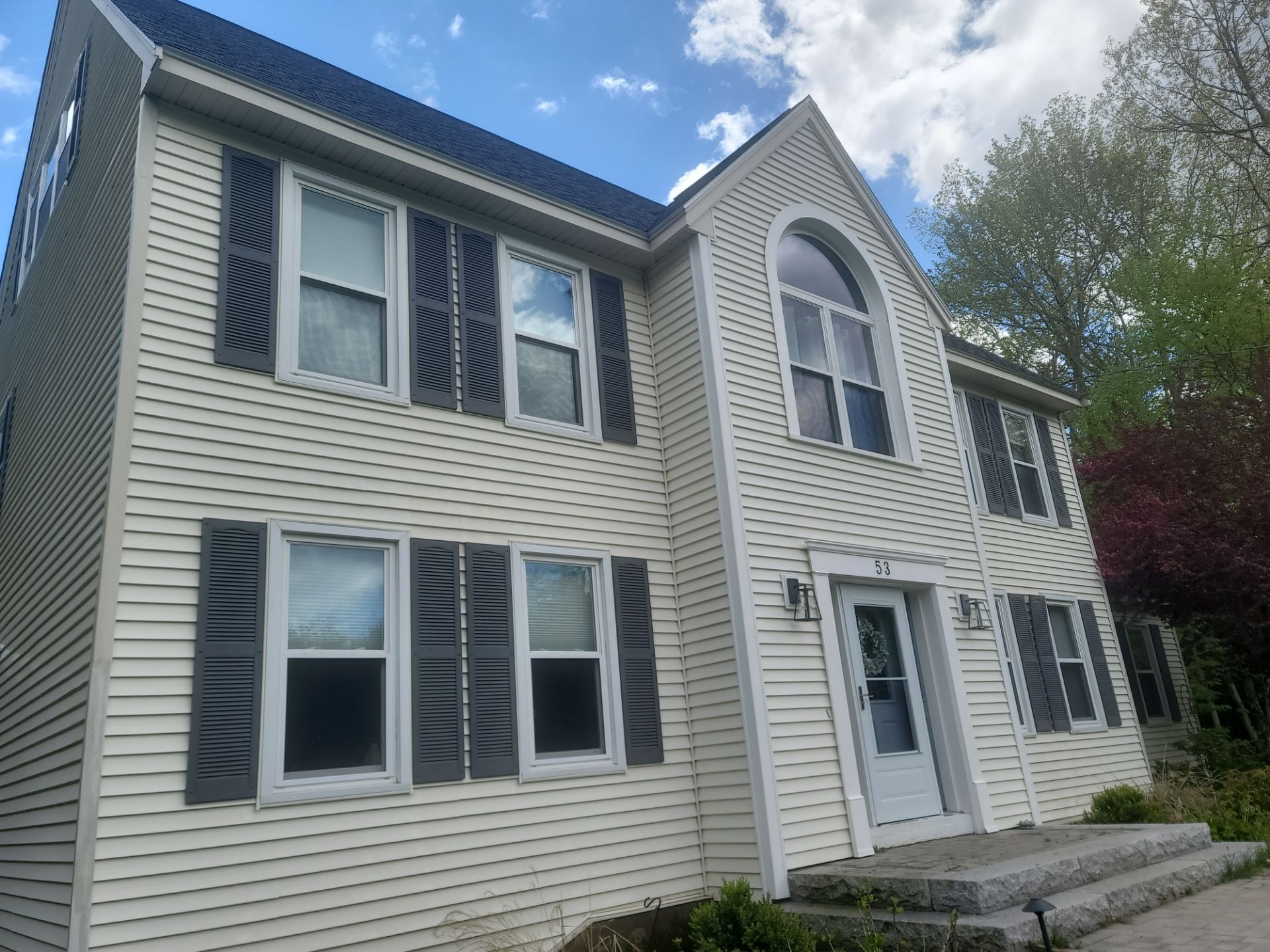 Two-story gray house with white trim, blue shutters, and a front porch under a partly cloudy sky