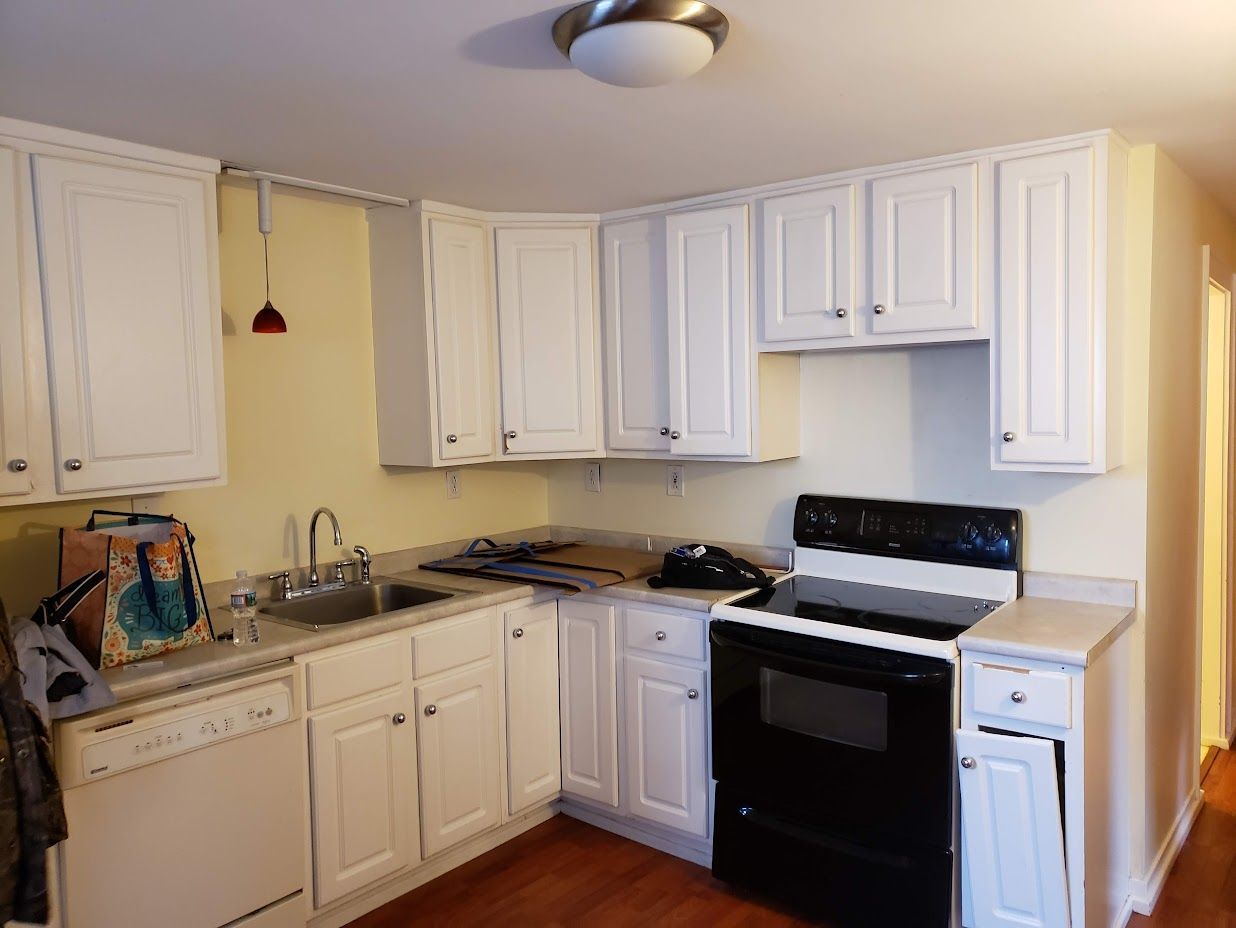 Compact white kitchen with black stove and sink, white cabinets, and yellow walls