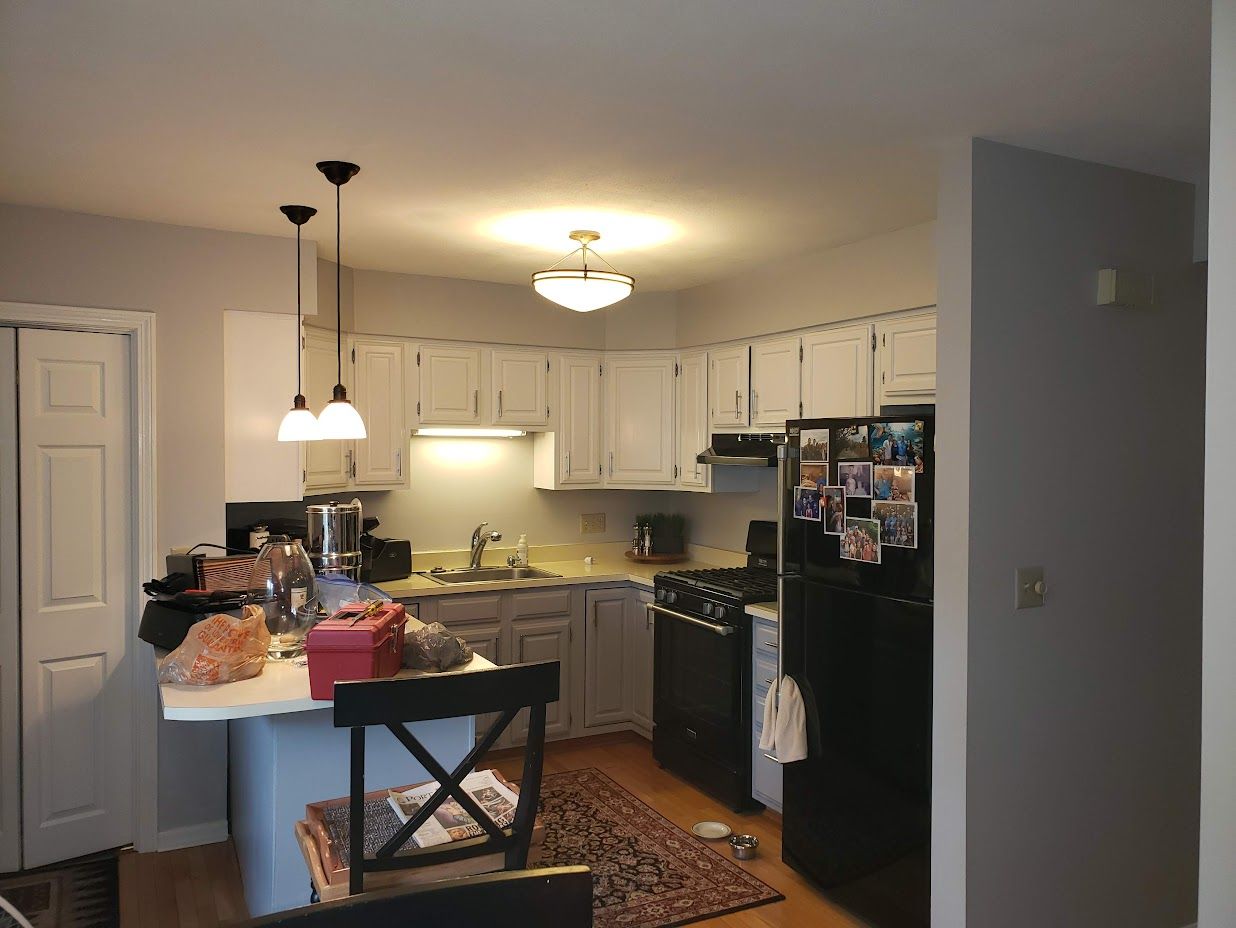 Kitchen with white cabinets, black appliances, island, hanging lights, and a patterned rug