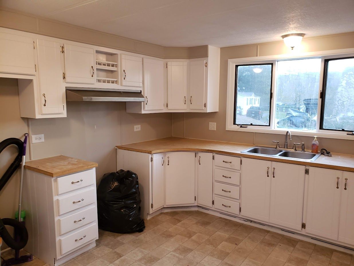 Small beige kitchen with white cabinets, wood countertops, stove, sink, and a large window.
