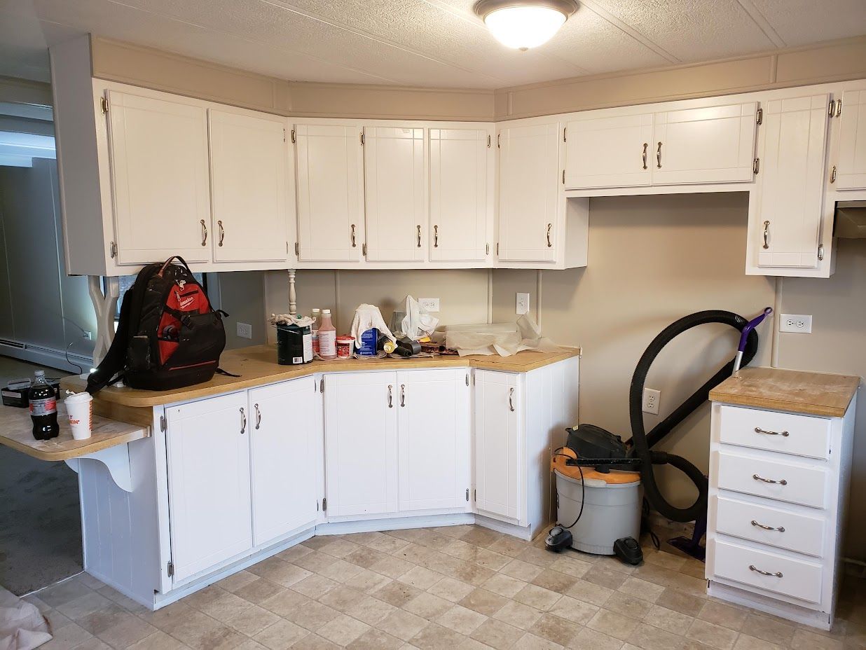 White kitchen with cabinets, countertop clutter, and a vacuum hose beside a small drawer unit