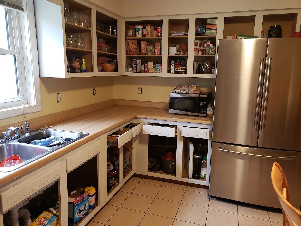Small kitchen with stainless-steel fridge, sink, beige counters, open cabinets, and tiled floor.