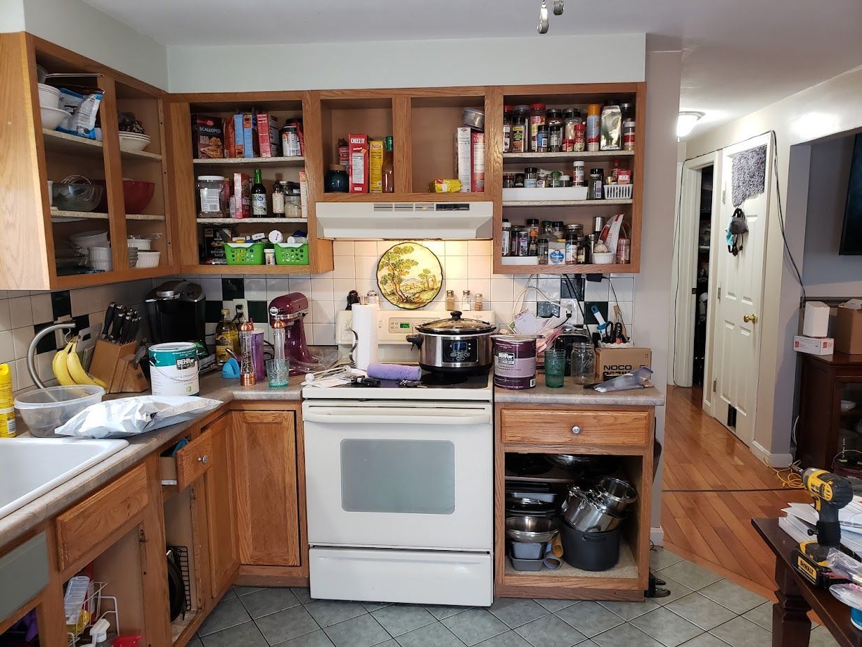 Cluttered kitchen with wooden cabinets, white stove, and countertop appliances in warm lighting.