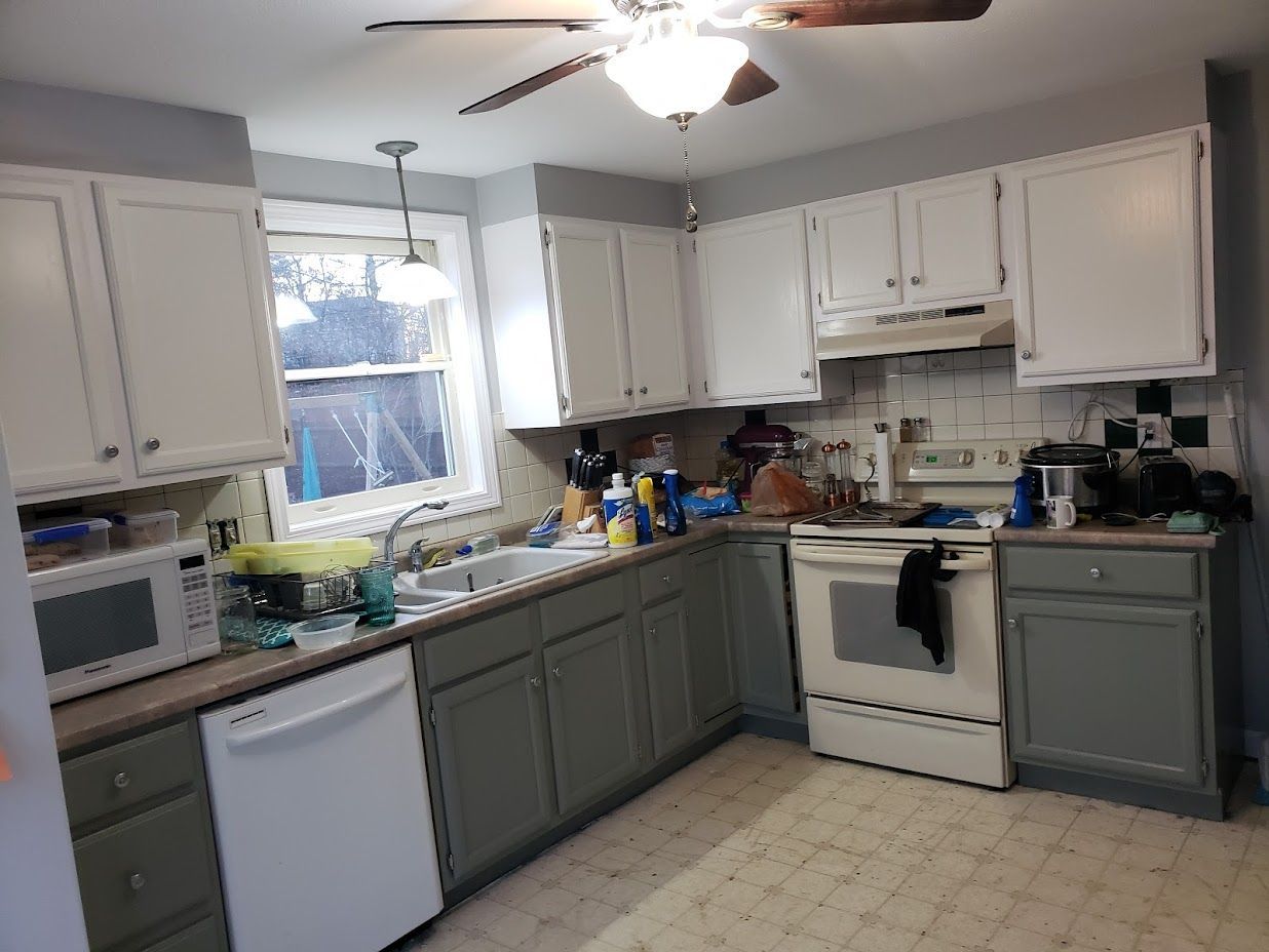 Small kitchen with white and gray cabinets, a ceiling fan, and a window over the sink.
