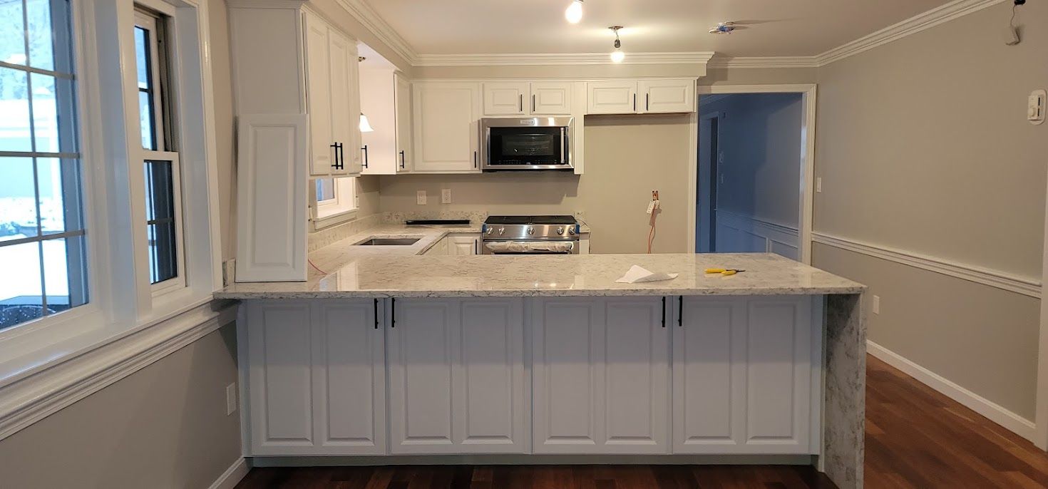 Empty modern kitchen with white cabinets, gray island, stainless stove, and hardwood floors