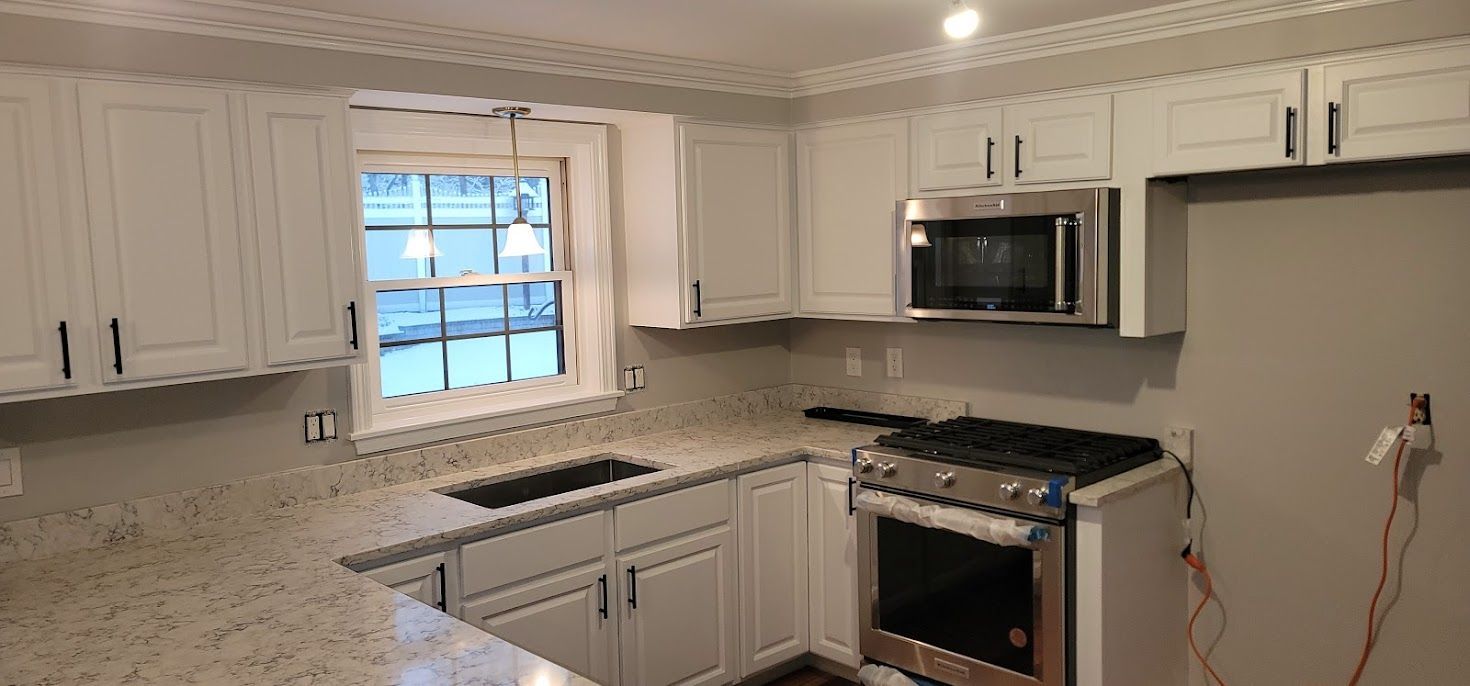 Bright white kitchen with granite counters, window, stainless steel stove and microwave, and a tiled backsplash